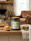Green  Grounded candle with a label on a wooden surface in a cozy living room setting.
