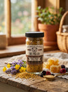 Jar of Big Bear Honey Bee Pollen on a wooden table with honeycomb and flowers.