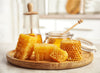 Honeycomb pieces and a jar of honey on a wooden plate with a blurred background