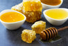 Honeycomb pieces and honey in small white bowls on a dark surface