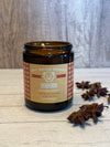 Bourbon scented candle in a glass jar with a label on a wooden surface, surrounded by star anise.