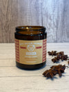 Bourbon scented candle in a glass jar with a label on a wooden surface, surrounded by star anise.