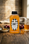 Bottle of Big Bear Honey on a wooden table with honeycomb pieces and plums.