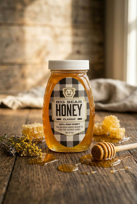 Jar of Big Bear Honey on a wooden surface with honeycomb and a honey dipper.