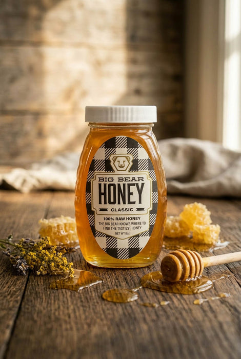 Jar of Big Bear Honey on a wooden surface with honeycomb and a honey dipper.