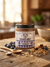 Jar of Big Bear Honey Blueberry Creamed Honey on a wooden table with blueberries and oats.