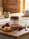 Jar of Big Bear Honey Creamed Honey Cherry on a wooden table with cherries and honeycomb.