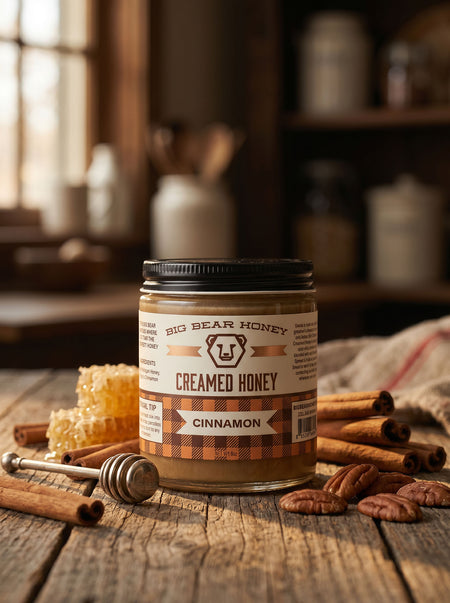 Jar of Big Bear Honey Creamed Honey Cinnamon on a wooden surface with honeycomb and cinnamon sticks.