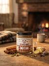 Jar of Big Bear Honey Spiced Chai on a wooden table with cinnamon sticks and a cup in the background.