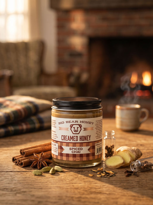 Jar of Big Bear Honey Spiced Chai on a wooden table with cinnamon sticks and a cup in the background.