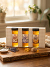 Three jars of honey in a wooden gift box on a wooden surface with lavender and honeycomb.