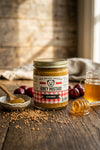 Jar of Honey Mustard with cherry flavor on a wooden table with honey and mustard seeds.