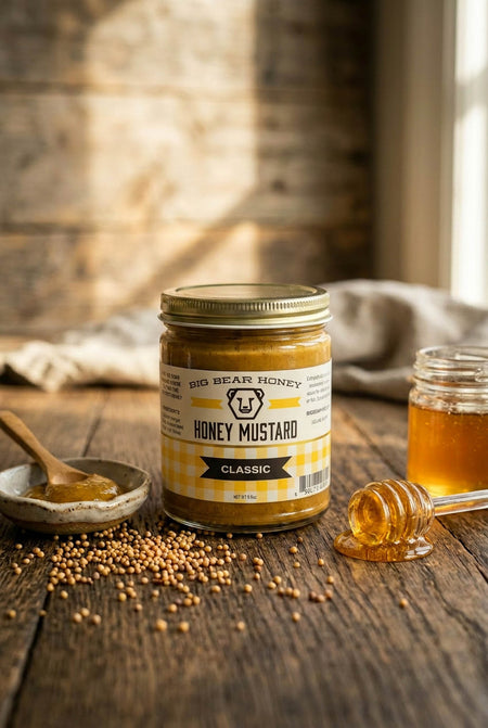 Jar of honey mustard on a wooden table with honeycomb and mustard seeds.