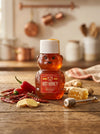 Hot Honey bear-shaped bottle on a wooden surface with spices and honeycomb in a kitchen setting