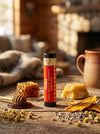 Mango lip balm tube on a wooden surface with honey, honeycomb, and herbs.