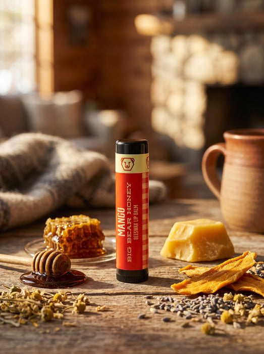 Mango lip balm tube on a wooden surface with honey, honeycomb, and herbs.