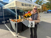Woman holding a bag of honey at a Big Bear Honey stand in a parking lot.