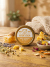Nature's Balm for dry hands and feet on a wooden surface with honeycomb, lavender, and other natural elements.
