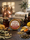 Big Bear Honey Nature's Balm for sore joints and muscles on a wooden surface with honey, lemons, and herbs.
