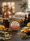 Big Bear Honey Nature's Balm for sore joints and muscles on a wooden surface with honey, lemons, and herbs.