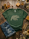 Green t-shirt with bear graphic and 'Michigan' text on a wooden surface with rustic items.