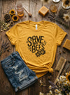 Yellow t-shirt with 'Save the Bees' text on a wooden surface with natural elements.