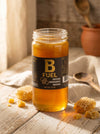 Jar of B Fuel honey on a wooden surface with honeycomb pieces.