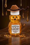 Honey bear bottle with a cowboy hat on a wooden surface with honey drizzling.
