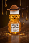 Honey bear bottle with a cowboy hat on a wooden surface with honey drizzling.