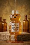 Honey bear bottle with honey dripping, surrounded by vintage bottles on a wooden surface.