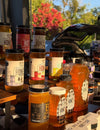 Jars of honey from various brands displayed outdoors with a blurred background