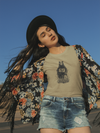 Woman wearing a floral jacket, beige t-shirt with a graphic, and denim shorts against a clear blue sky.